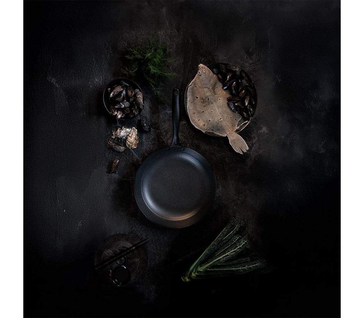 Stekpanna Satake Lättviktsgjutjärn Ø28cm med ingredienser och örter på mörk bakgrund
