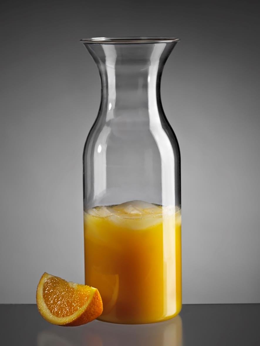 Transparent polykarbonatkaraff med orangejuice och en apelsinhalva framför