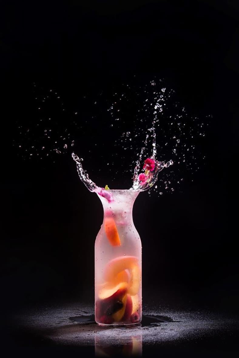 Karaff i polykarbonat transparent fyllt med vatten och frukt, med vattenstänk mot svart bakgrund