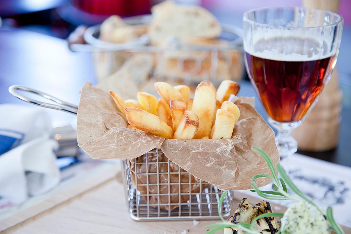 Minikorg med pommes frites i ett metallnät, bakgrund av ett glas rödvin och bröd på bordet
