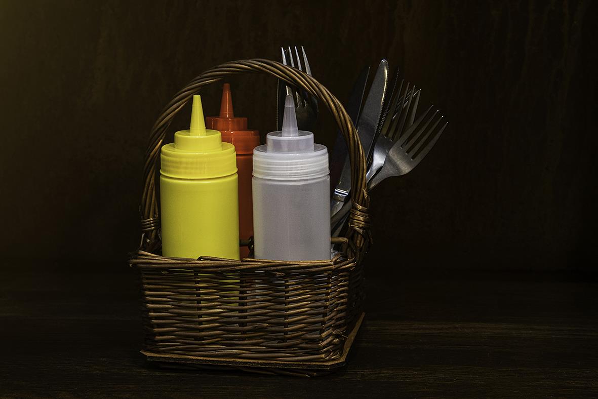 Kryddkorg med fyra fack och olika såser i en korg på en mörk bakgrund