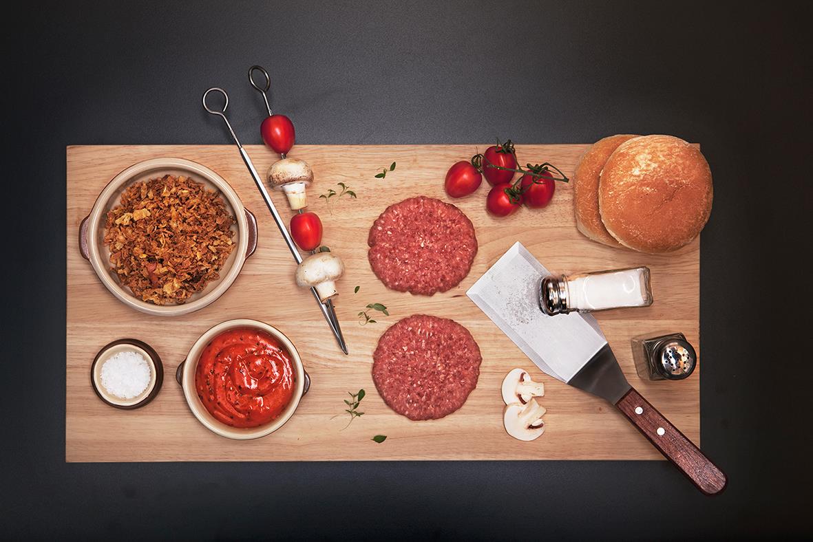 Grillspett, köttfärsbiffar, bröd, tomater, såser och kryddor på träskärbräda