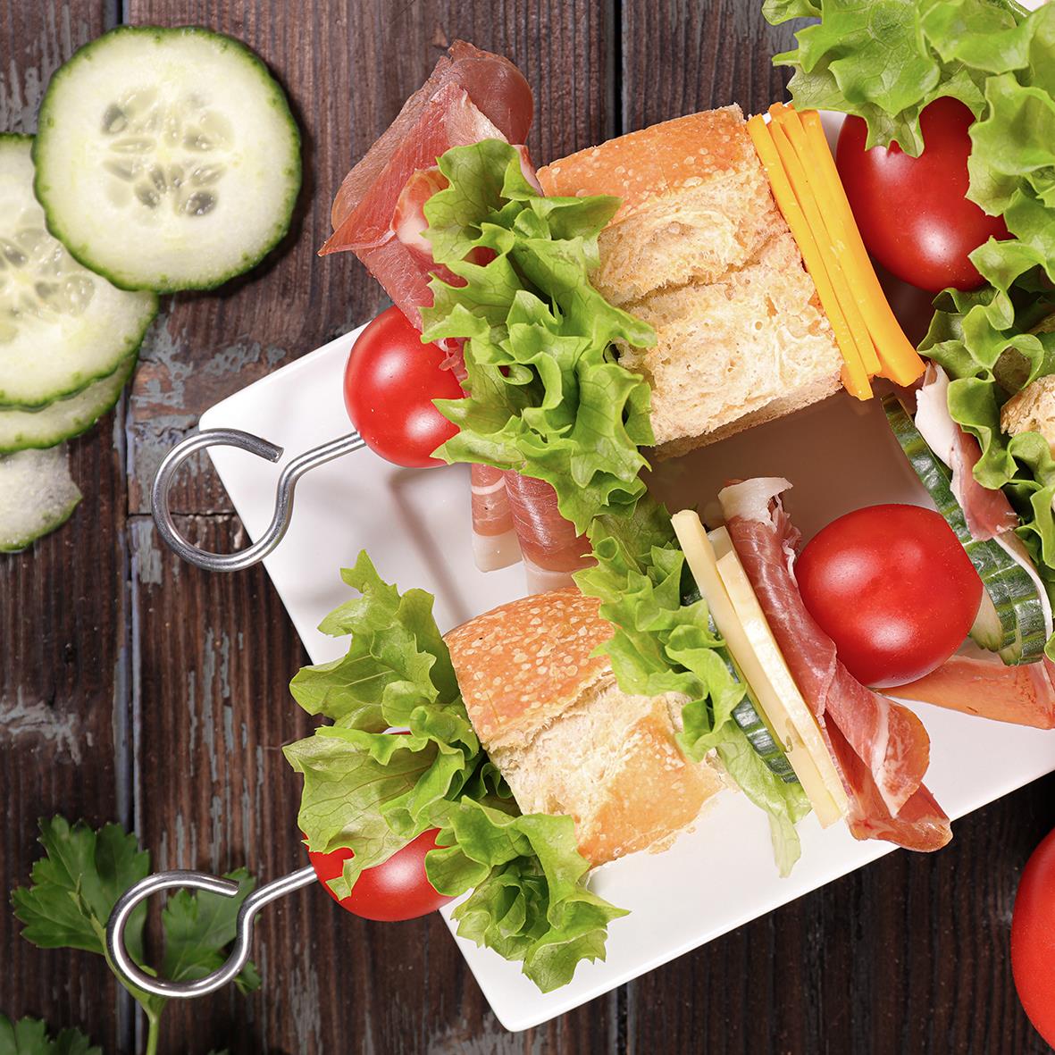 Två grillspett med kött, sallad, tomater och bröd på en vit tallrik