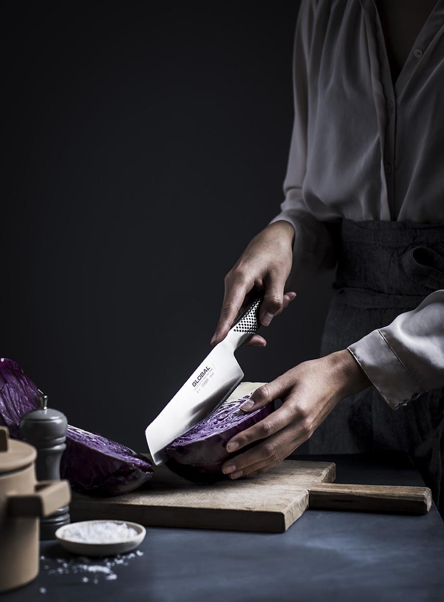 Person skär en aubergine med en grönsakshacka på en träskärbräda