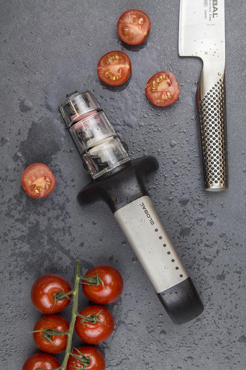 Knivslip Global G-91/SB med tomater och en kökskniv på en mörk yta