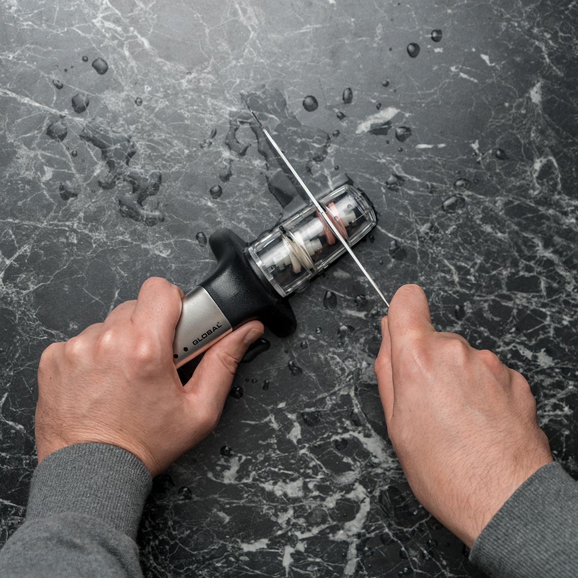 Person slipar en kniv med en elektrisk knivslip på en mörk marmorgolv