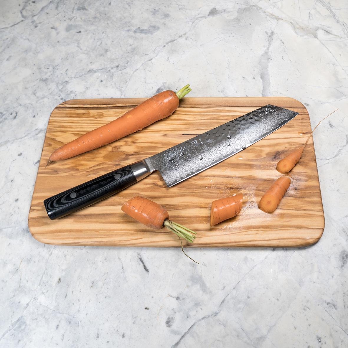 Kockkniv på träskärbräda med morötter och ett par små morötter