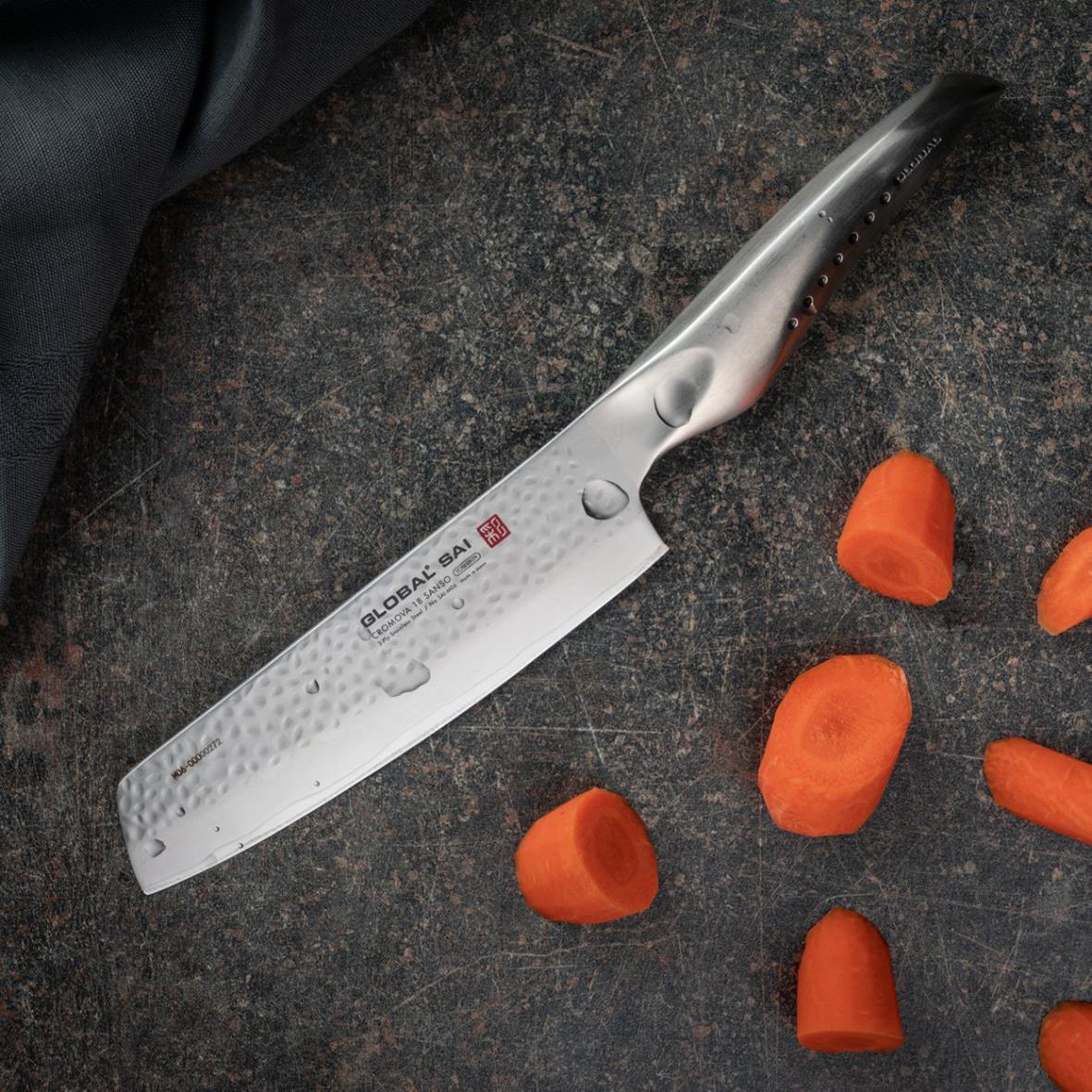 Kockig kniv med svart och silverhandtag bredvid skurna morötter på mörk yta