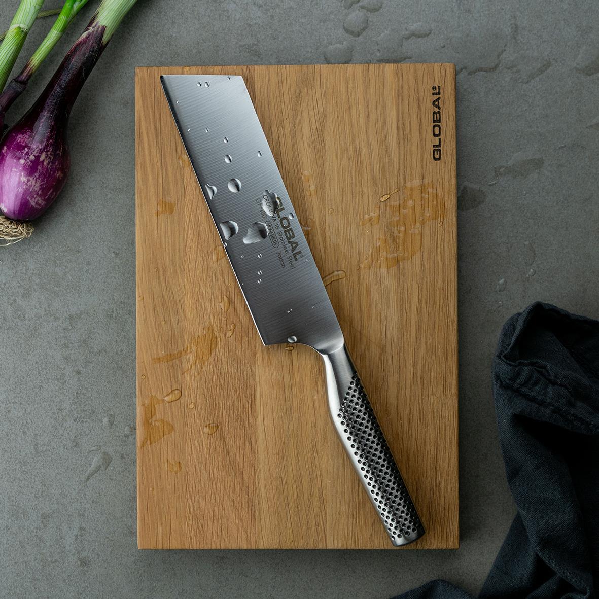 Grönsakshacka från Global GF-100 18cm på träskiva med lök och svart tyg i bakgrunden