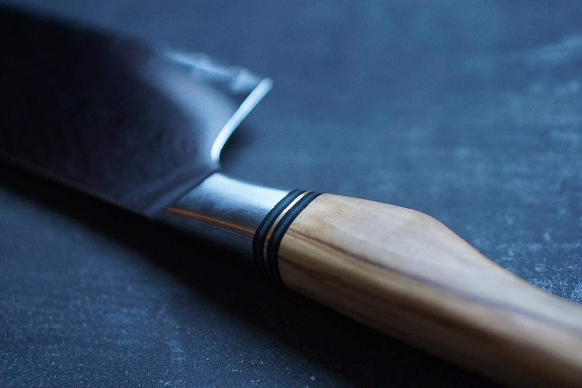 Kockkniv med trähandtag och svart blad liggande på mörk bakgrund