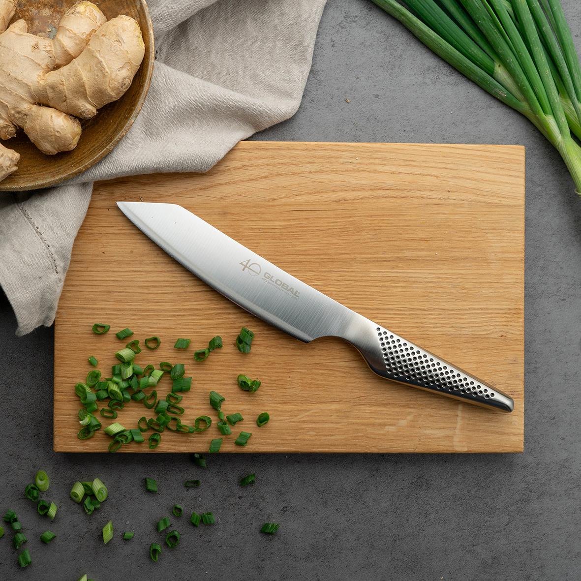 Kockkniv Kiritsuke Global 40-års Jubileum GS-110 15cm på träskärbräda med grönsaker och ingefära
