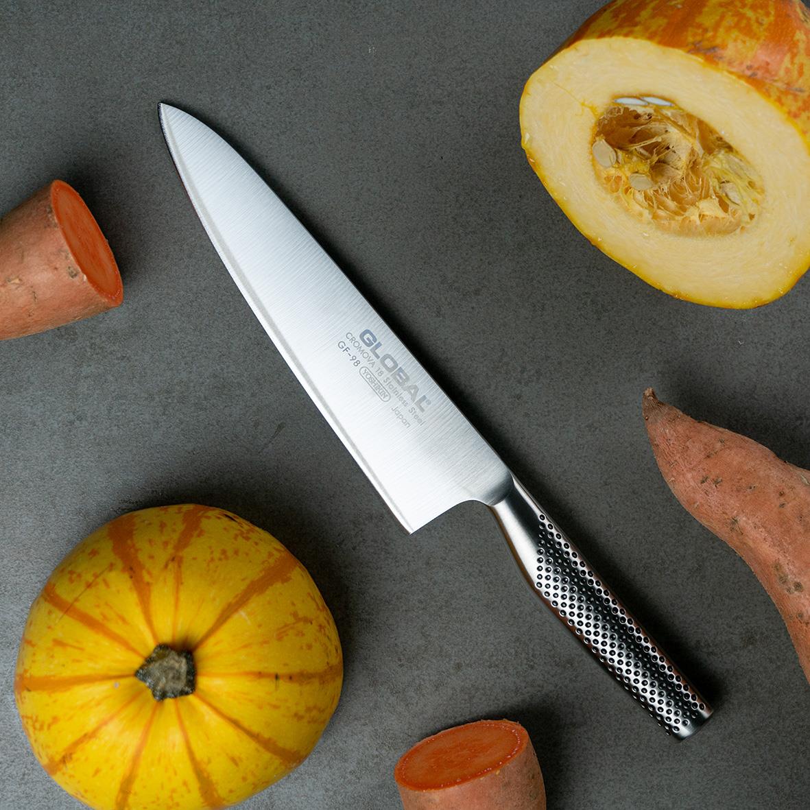 Kockkniv Global GF-98 20,5cm smidd med svart skaft, omgiven av pumpa och rotfrukter