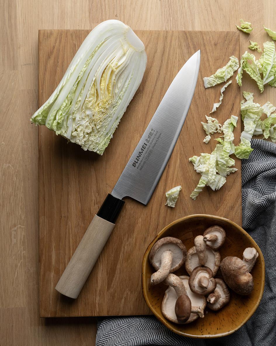 Kockkniv Bunmei 20cm på träskärbräda med sallad och svamp