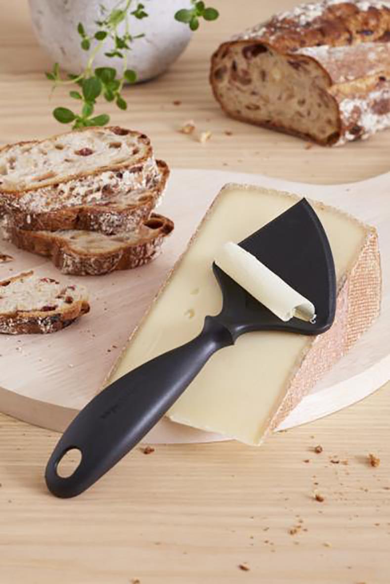 Osthyvel Gastromax plast svart på en ost med bröd och växt i bakgrunden