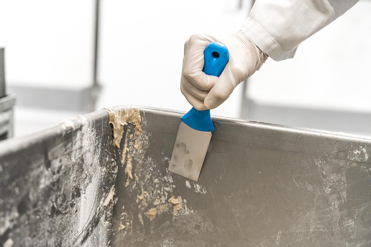 Person använder en blå rostfri handskrapa på en metallskål