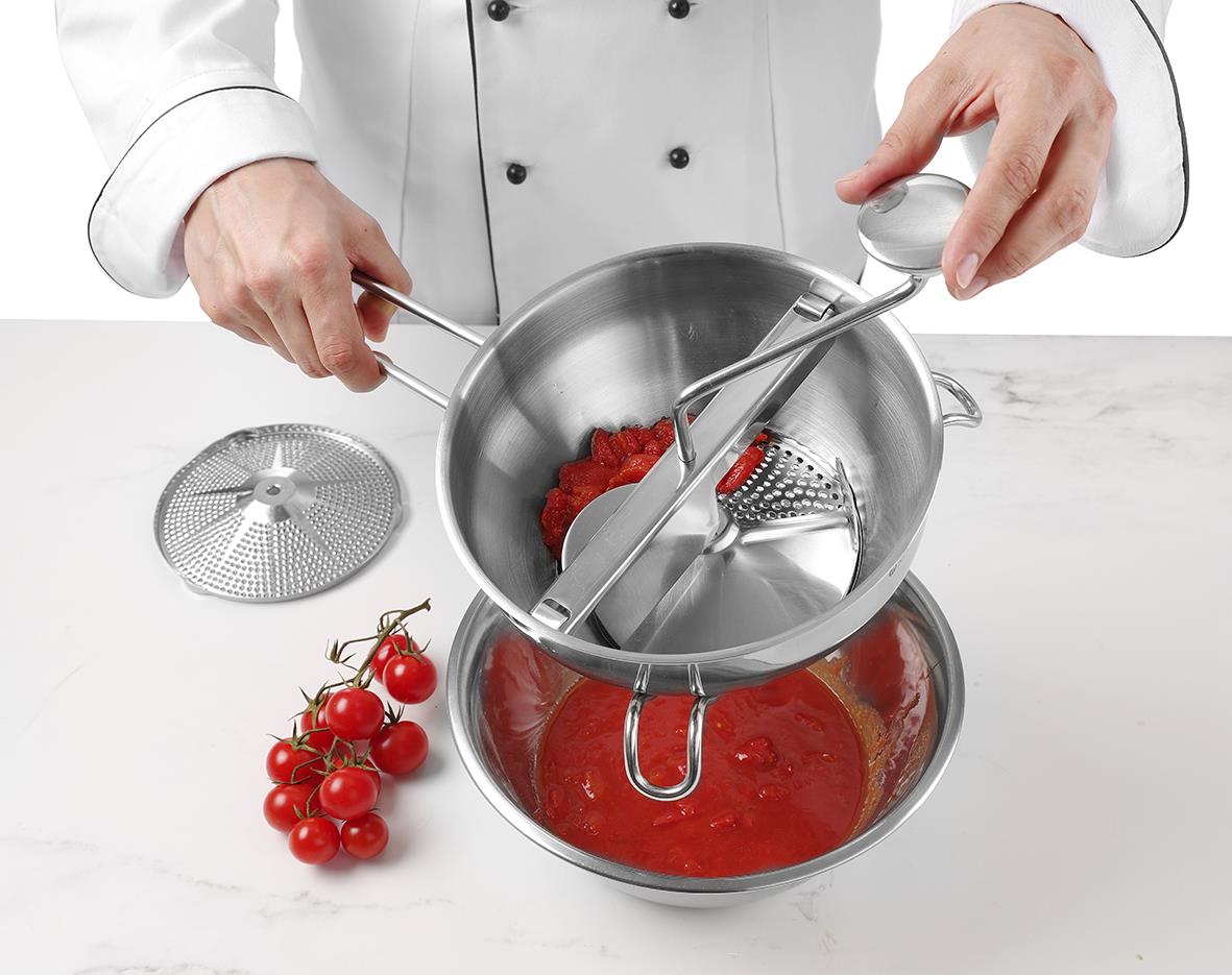 Person som använder passör Hendi för att sila tomatsås, med tomater och passör i köket