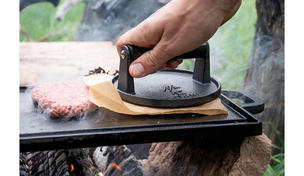 Person använder en smidesjärn Satake utomhus för att pressa kött på en grill