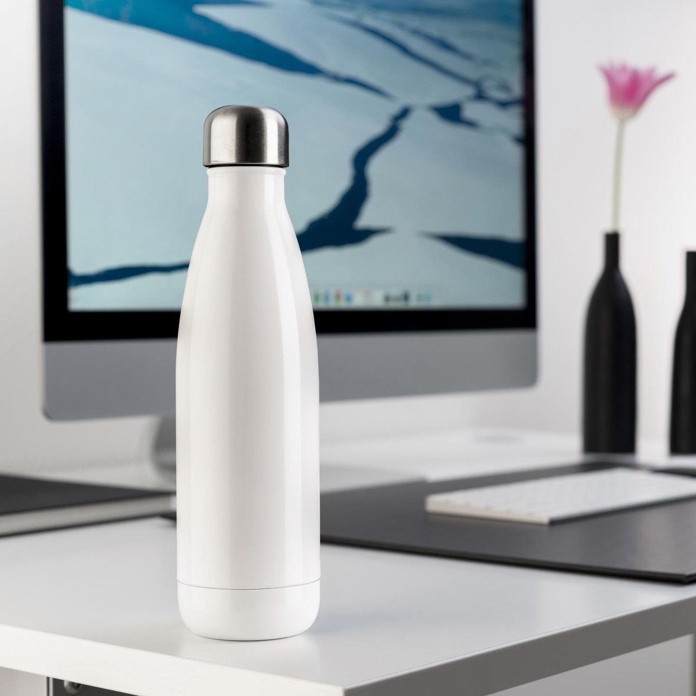 Vit vattenflaska JobOut 500ml stående på skrivbord framför dator och blomma i vacker vas