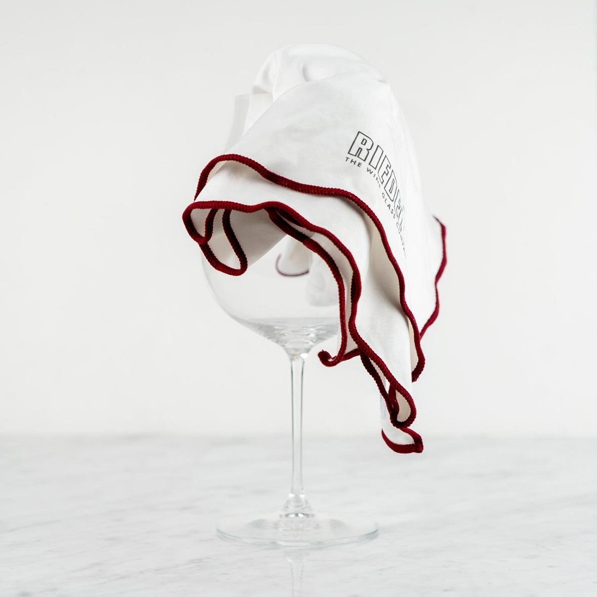 Vit putsduk med Riedel-logga hängande över ett tomt vinglas