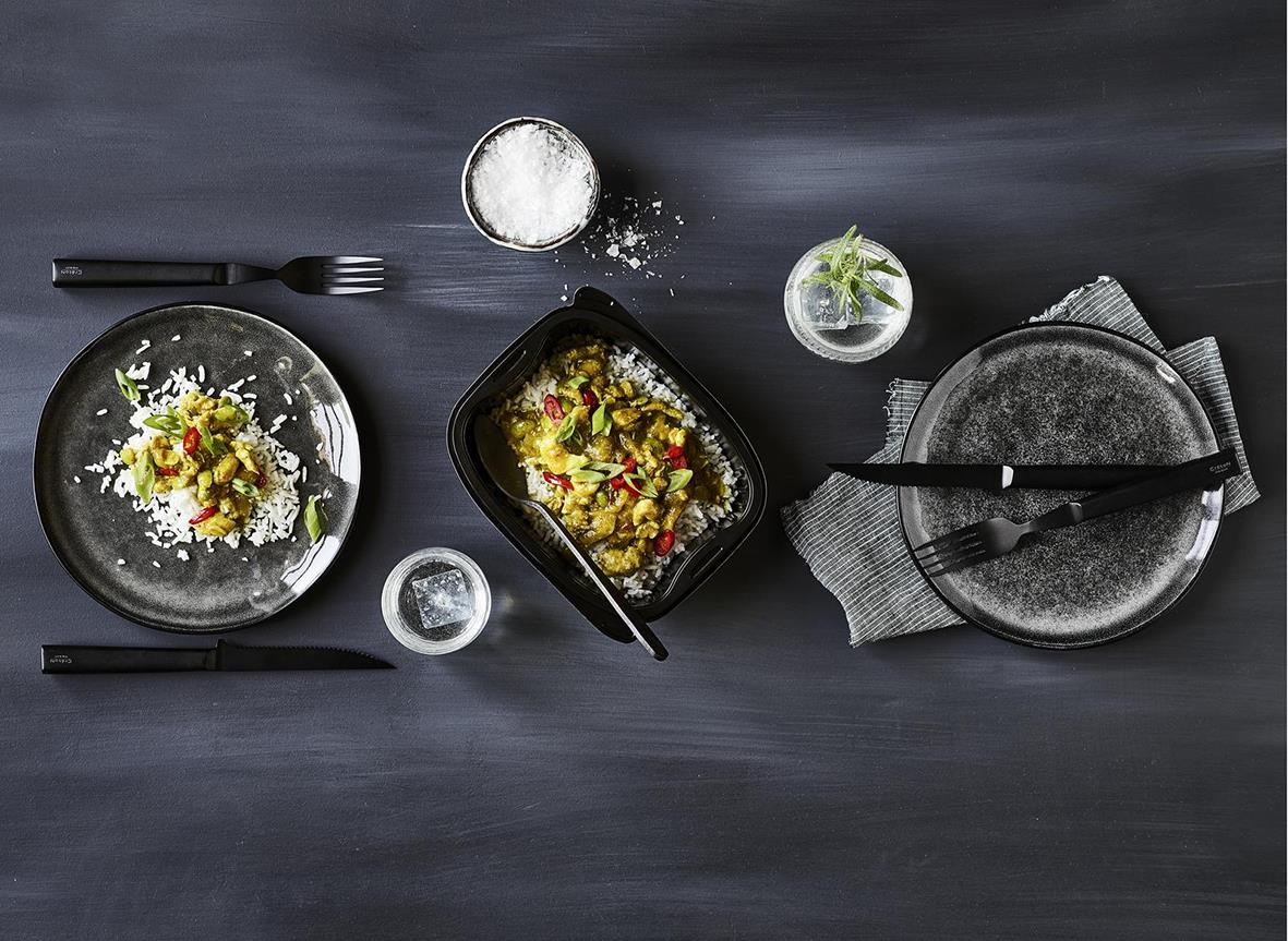 Svart plastbägare med mat, bestick, salt och kryddor på mörk bakgrund