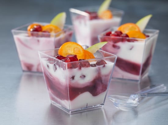 Tre fyrkantiga klara plastbägare fyllda med dessert, dekorerade med frukt