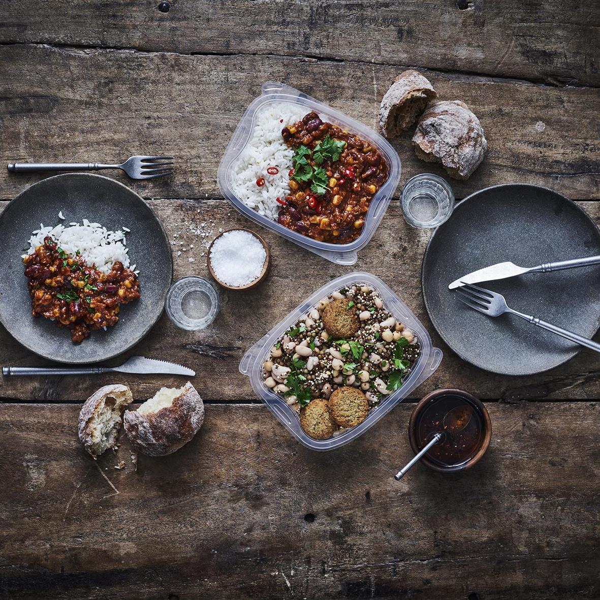 Plastform Bistro PP klara matlådor med mat på ett träbord, omgivna av bröd och drycker