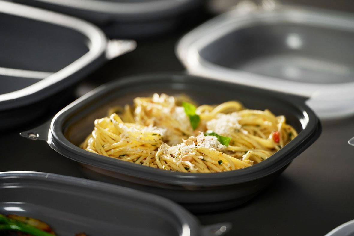 Färdiglagad pasta i en svart matlåda med parmesan och grönt, redo att äta