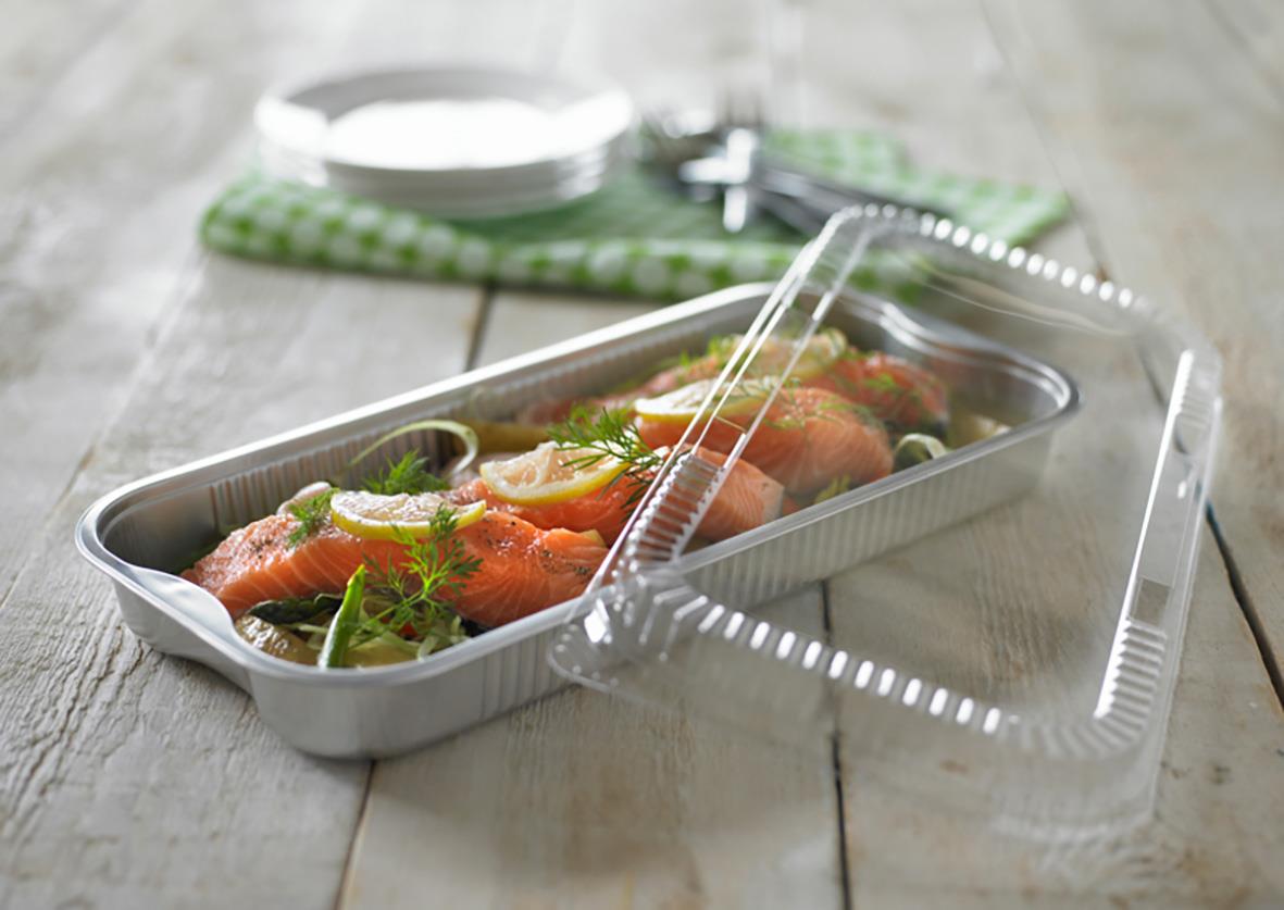 Aluminiumform med lax och grönsaker, täckt med transparent lock, på träbord