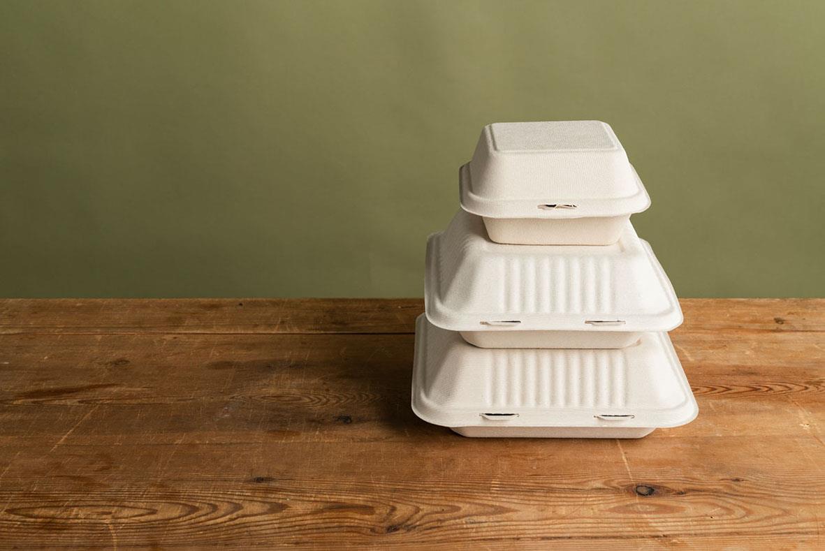 Hämtbox Duni Bagasse Hinged Brun 225x201x85mm med mat och tillbehör i en öppen låda på träbord
