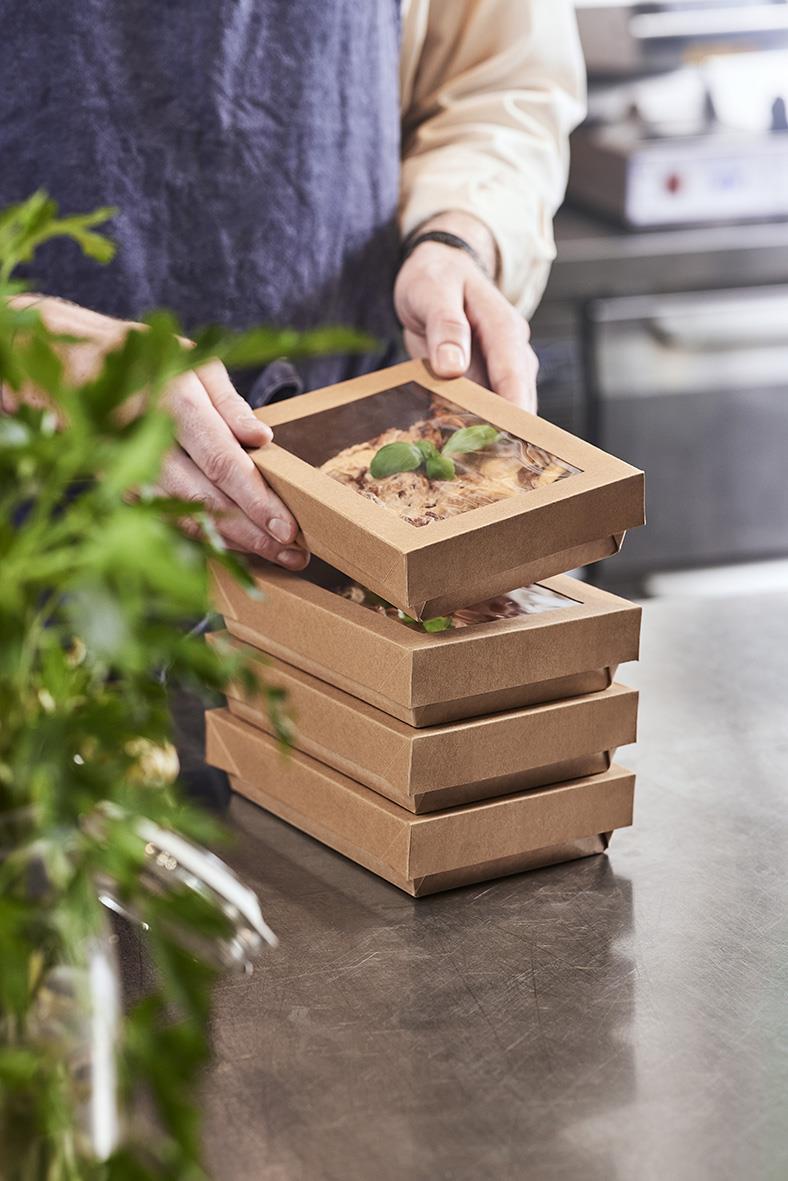 Person placerar lådor med fönster och växtmotiv på ett bord i ett kök