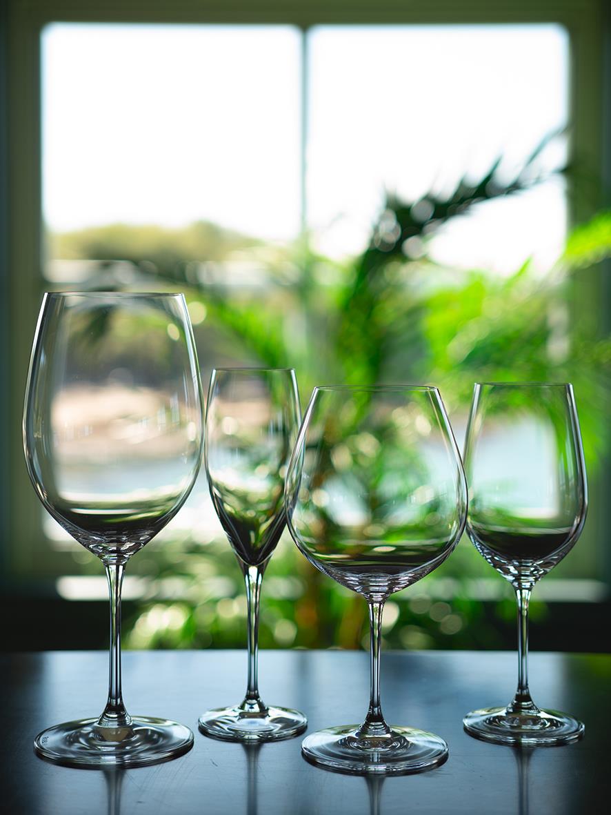 Fyra vinglas av Riedel Vinum Zinfandel/Riesling modell på ett bord framför ett fönster med gröna växter i bakgrunden