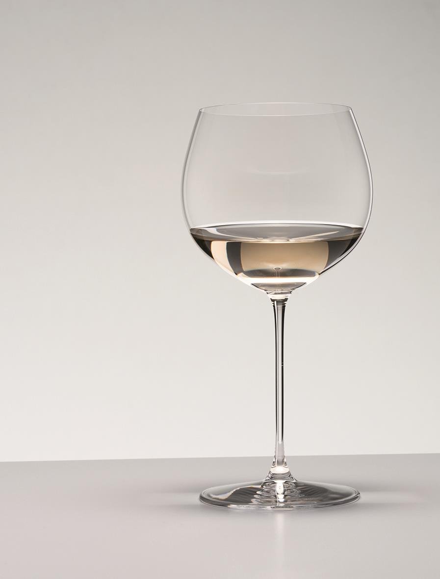 Vinglas Riedel Veritas Oaked Chardonnay med lång stjälk och rund kupa, fyllt med vitt vin, mot en neutral bakgrund