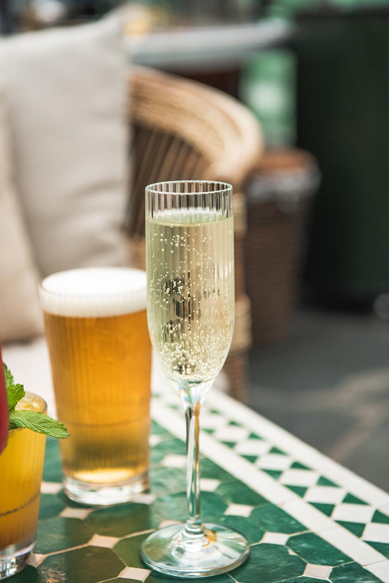Champagneglas av polykarbonat med stripe-mönster, fyllt med mousserande vin, på ett grönt och vitt bord