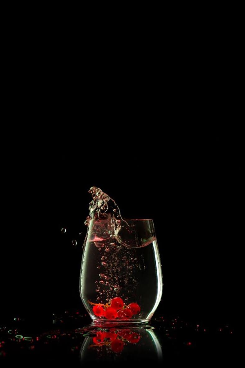 Vattenglas utan fot med röda bär som fylls med vatten och bubblor, mot svart bakgrund