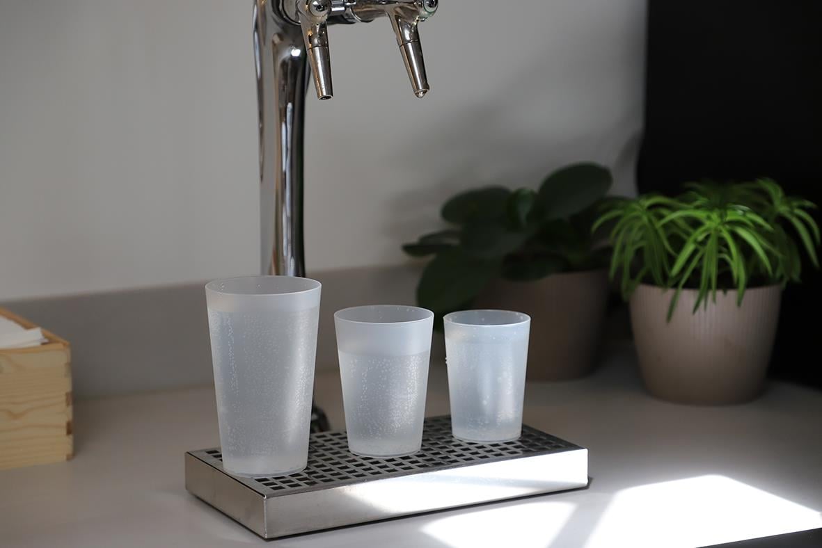 Tre frostade vattenglas av plast på ett serveringsställ med växter i bakgrunden