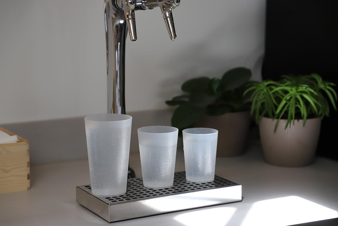 Tre frostade vattenglas av plast på en metallbricka med växter i bakgrunden