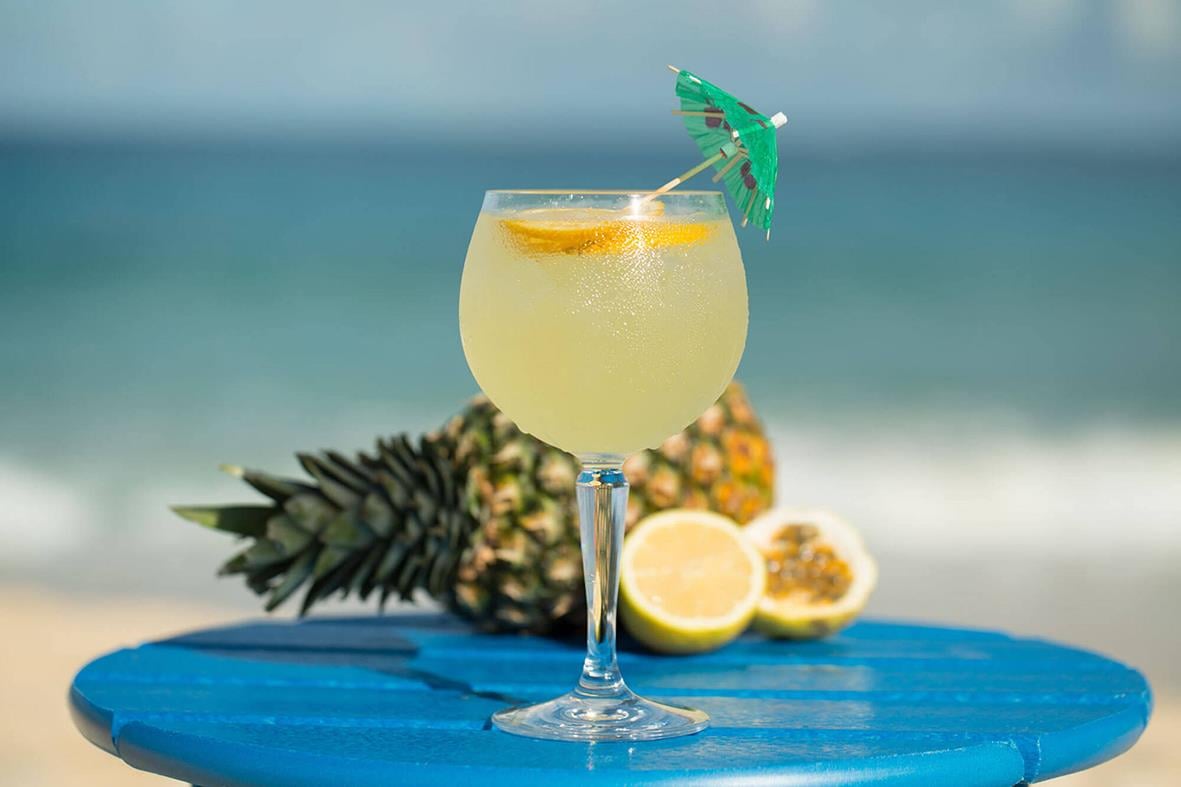 Gin & Tonicglas av polykarbonat med citron och liten parasoll på blå yta vid stranden
