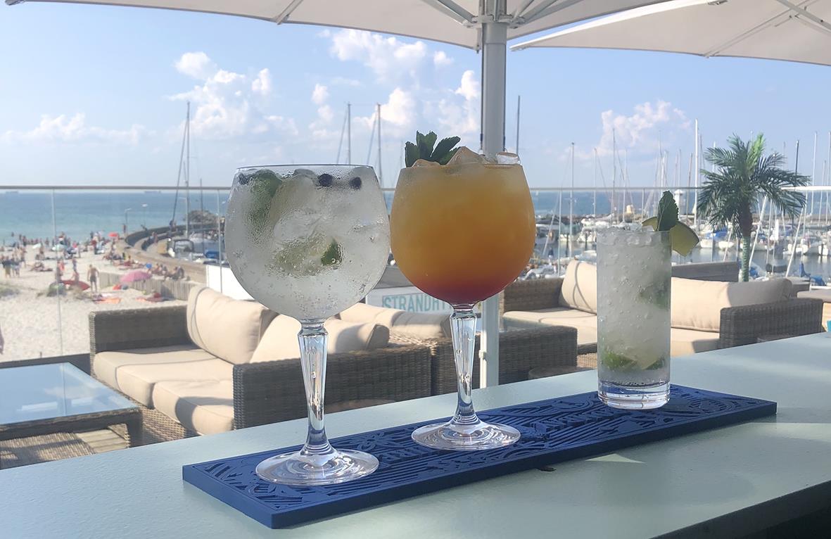 Två gin & tonicglas och ett vattenglas på en barbänk med havsutsikt och båtar i bakgrunden