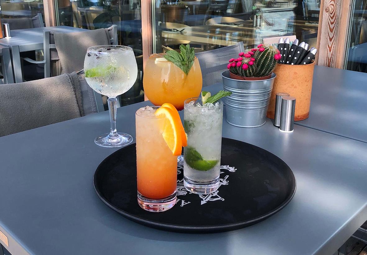 Tre färgglada drinkar på svart serveringsbricka på bord utomhus