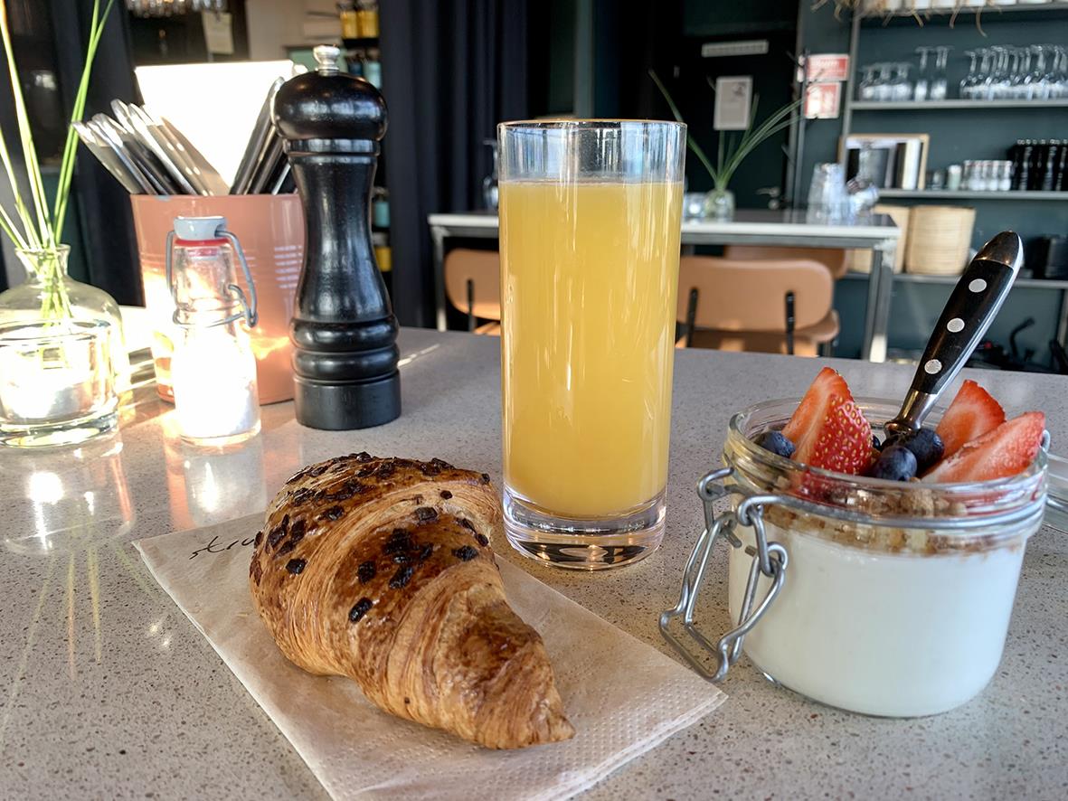 Drinkglas Falsterbo i polykarbonat med juice, croissant och yoghurt med bär på ett cafébord