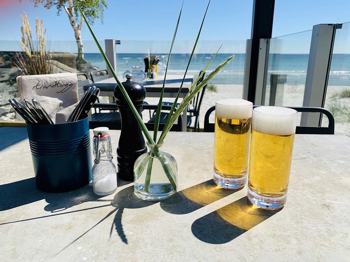 " ölglas med öl på ett bord vid stranden, bakgrund av hav och klar himmel"