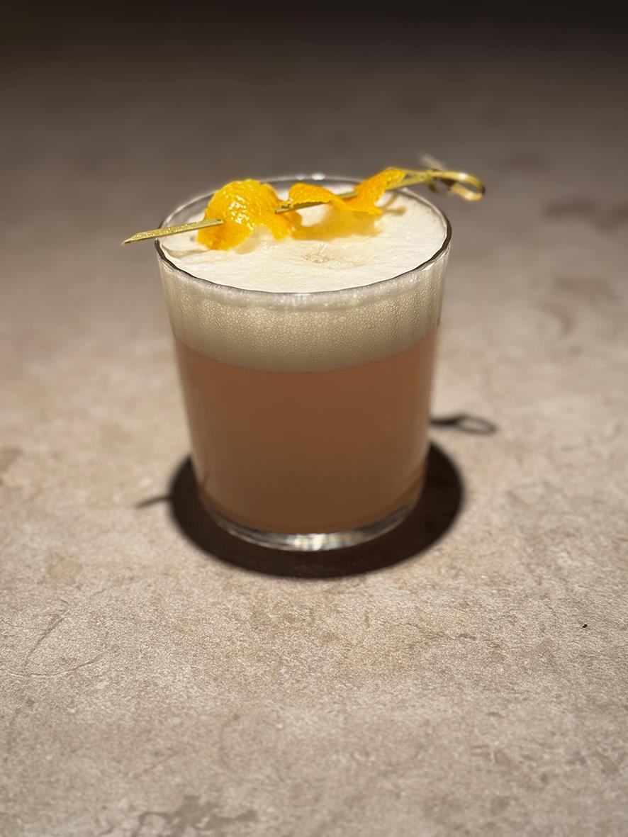 Drinkglas med cocktail, dekorerad med citronzest, på en neutral yta
