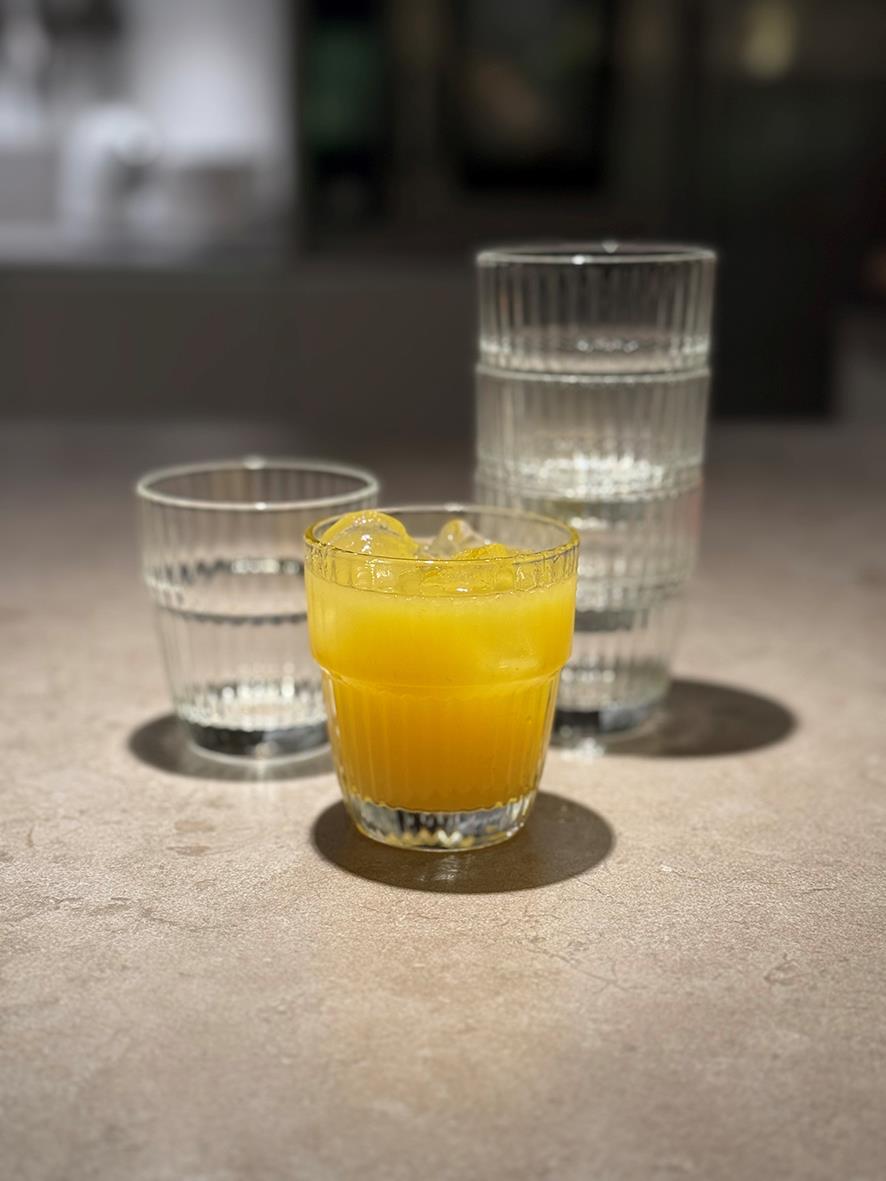 Vattenglas och ett litet glas med orange juice på en grå yta, bakgrund av två större vattenglas