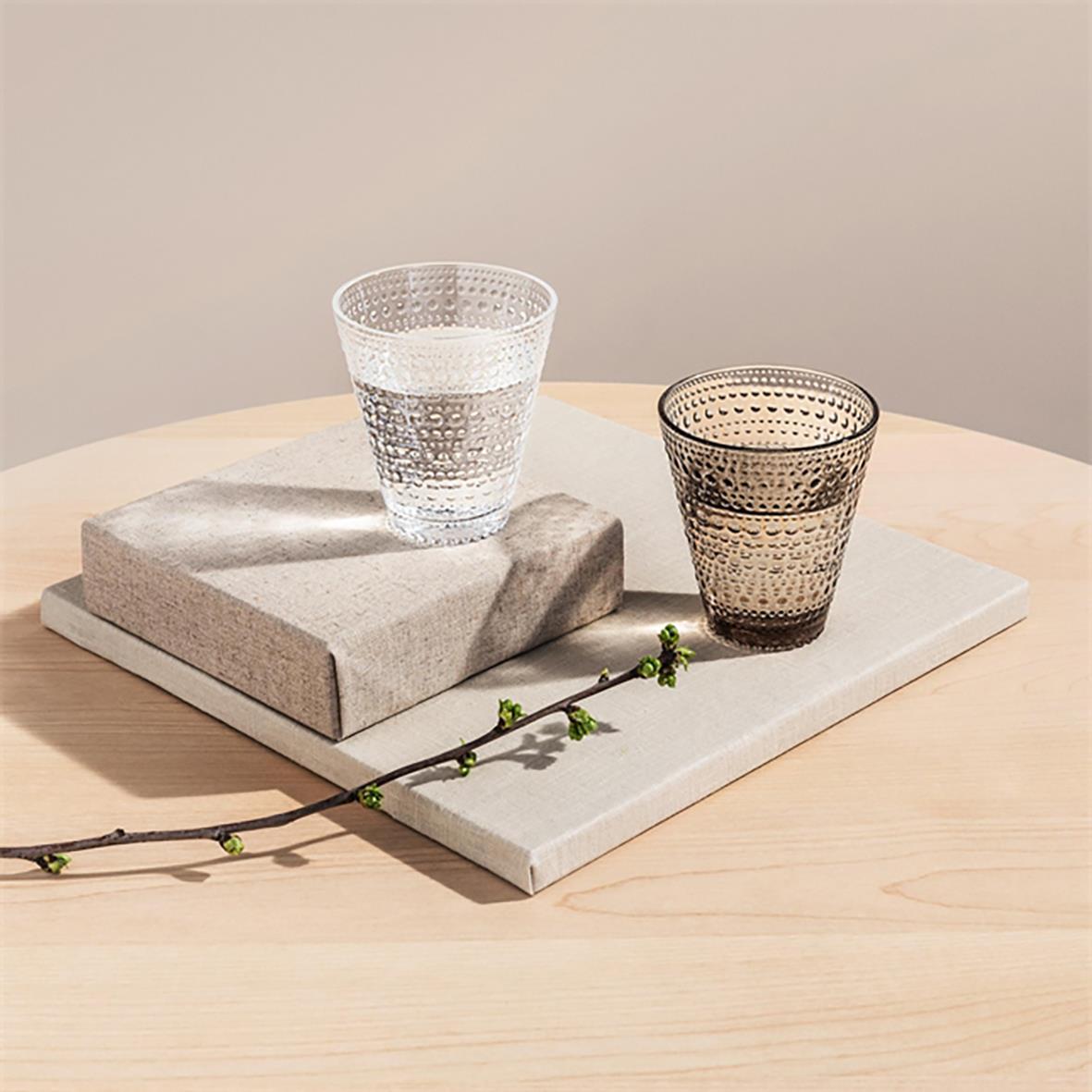 Två Iittala Kastehelmi glas, ett klart och ett mörkt, på en marmorskiva med en blomkvist framför