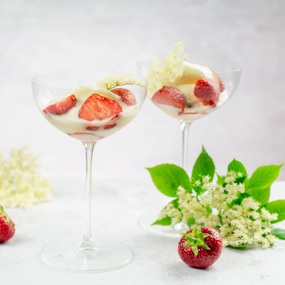 Två cocktailglas med jordgubbar och grädde, dekorerade med gröna blad och vita blommor