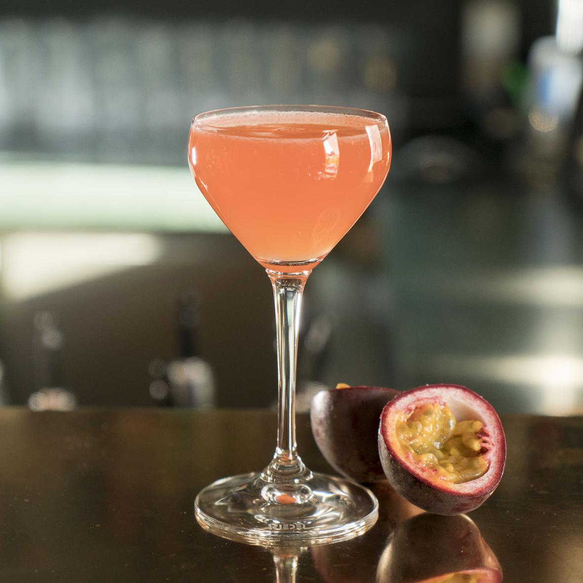 Cocktailglas från Riedel med rosa drink och en halverad passionsfrukt på en bar