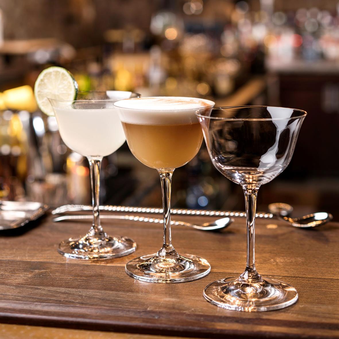 Tre cocktailglas på barbord, ett med limeklyfta, i bakgrunden barmiljö
