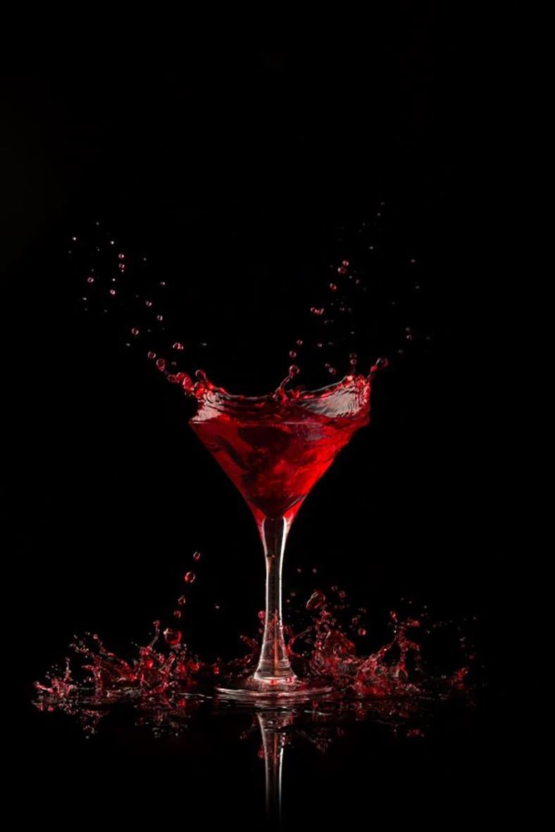 Martiniglas i polykarbonat med röd dryck och vattenstänk mot svart bakgrund