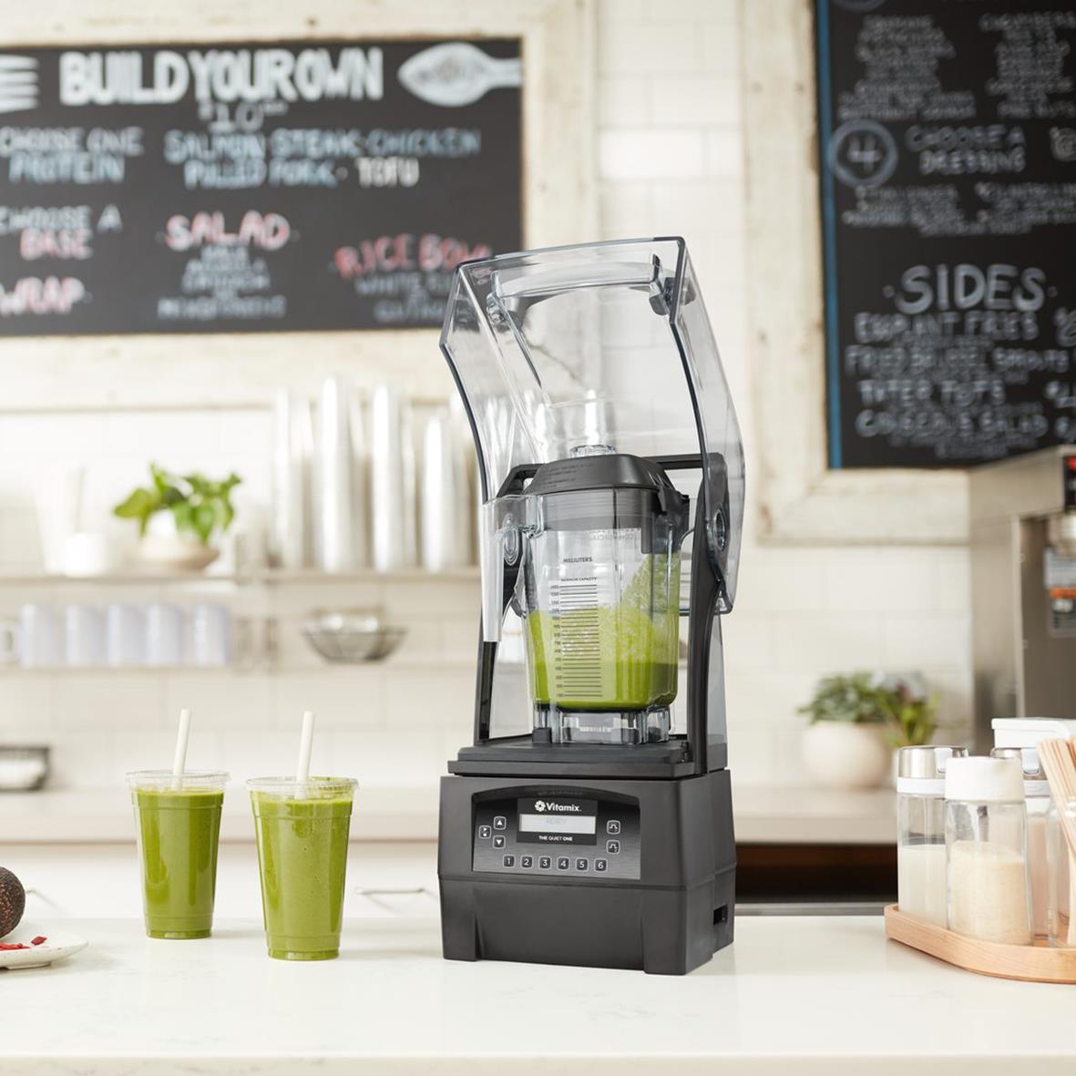 Vitt Vitamix Blender The Quiet One på köksbänk med två gröna smoothies och bakgrund av köksutrustning