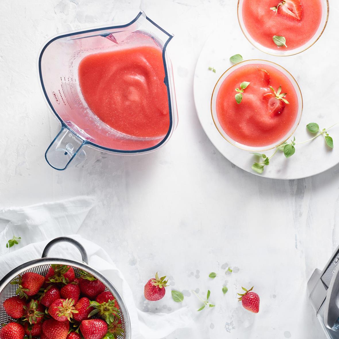 Vitamix Blender The Quiet One med en skål med tomatsop och en skål med jordgubbar på ett vitt bord